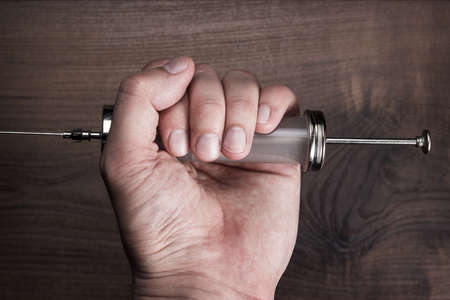 man holding syringe over brown wooden backgroundの写真素材