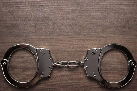 steel handcuffs on the brown wooden backgroundの写真素材
