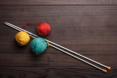 knitting needles and colorful ball of threads on the wooden background