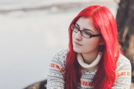 beautiful red-haired woman sitting near the riverの写真素材