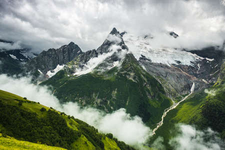 mountains with green grass snow and stormy sky landscapeの写真素材