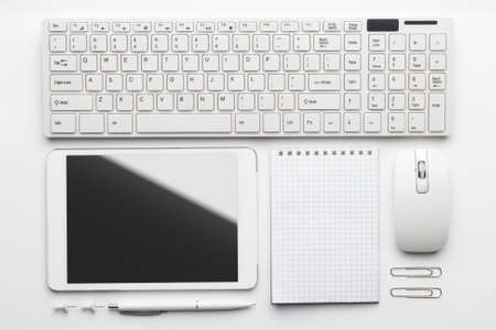 overhead of essential office objects in order on white desk. notebook, computer keyboard and mouse,...