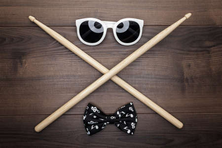 pair of wooden drumsticks crossed on wooden table, sunglasses and bow tieの写真素材