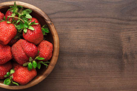 wooden bowl full of fresh strawberries on the brown tableの写真素材