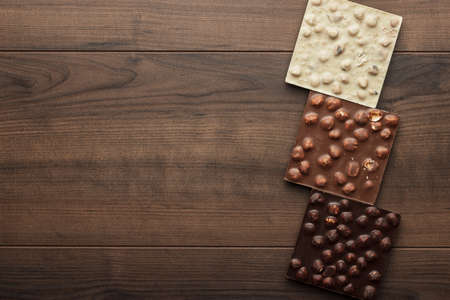 black, milk and white chocolate bars with whole hazelnuts on wooden tableの写真素材