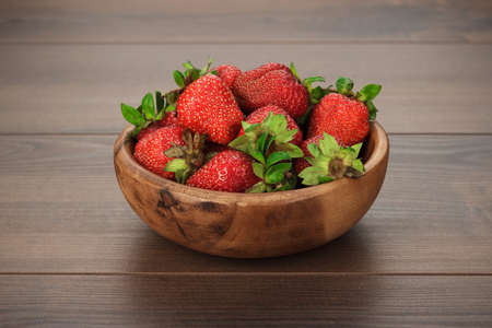 wooden bowl full of fresh strawberries on the brown tableの写真素材