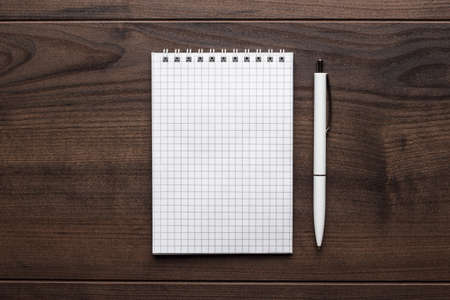 blank notebook and white pen on the brown wooden table