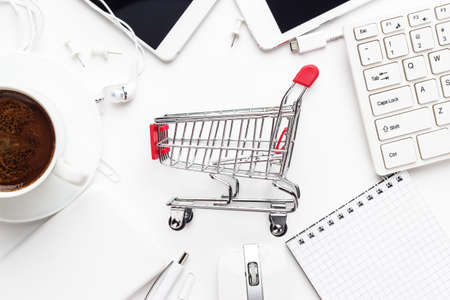 shopping online concept. small red trolley, different gadgets and stationery on the white office tableの写真素材
