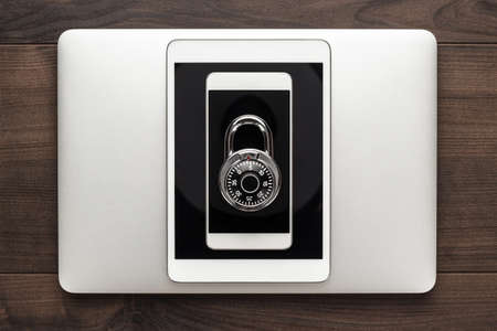 data security concept: computer, tablet, phone with combination lock on wooden tableの写真素材