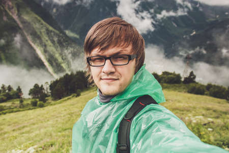 man in glasses taking selfie. mountains with green grass in backgroundの写真素材