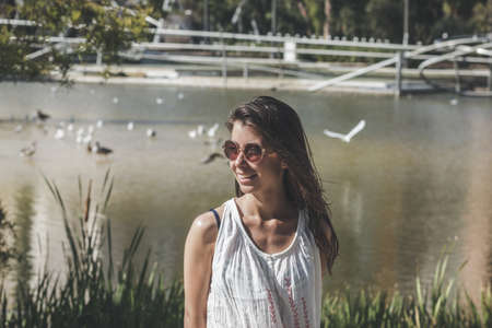portrait of young smiling woman with sunglasses in the park near the lakeの写真素材