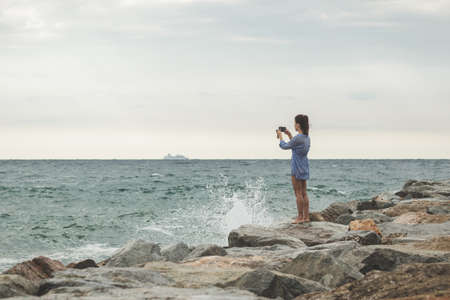 young woman taking photos of a ship in the ocean on her smartphone. travel smartphonographyの写真素材