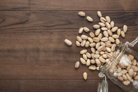 overturned glass jar full of roasted pistachios on the wooden table backgroundの写真素材