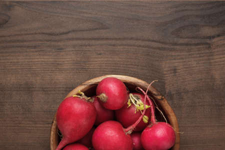 fresh red radishes in wooden bowl on the brown table with copy spaceの写真素材