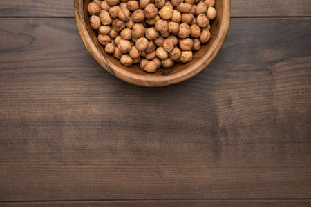 Photo of a bowl full of hazelnuts on the brown wooden table with copy spaceの写真素材