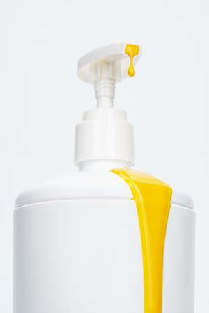 White soap dispenser close-up with yellow liquid dripping out of it