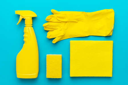 Yellow cleanser in plastic container with spray, rubber protective gloves, sponge and cloths for cleaning on the turquoise blueの写真素材