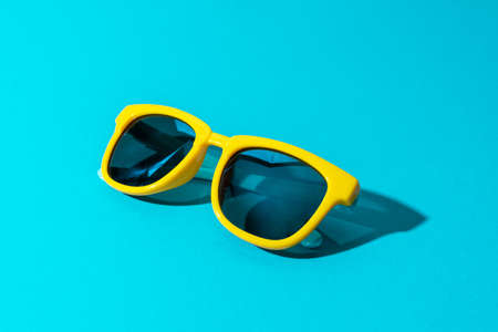 Close-up image of plastic sunglasses on turquoise blue background in perspective. Minimalist photo of stylish yellow sunglasses with harsh shadow as summer concept.の写真素材