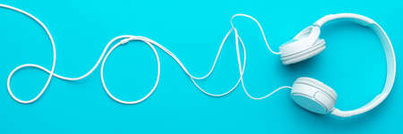 White headphones with cable. Top view of headphones on turquoise blue background. Minimalist photo of earphones with copy space. White dj headphones with cable in upper part of blue backgroundの写真素材