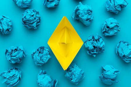 New idea concept with crumpled office paper and yellow paper ship. Top view of great business idea concept over blue background with yellow paper boat in the center.の写真素材