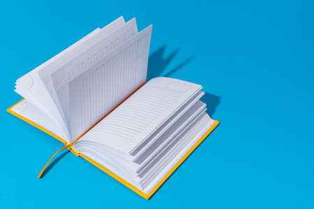 Photo of opened notebook on blue background with copy space. Minimalist image of blank diary in perspective. Stylish shot of a notebook with harsh light and shadow.の写真素材