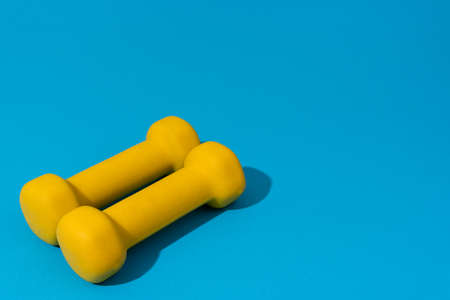 Photo of fitness dumbbells over blue backgound in perspective. Image of yellow dumbbells with copy space.の写真素材