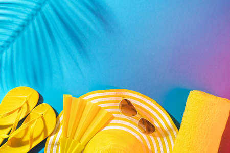 Yellow beach accessories on turquoise blue background - sunglasses, folding fan, towel, flip-flops and striped hat. Summer is coming concept with palm tree shadow and copy space.の写真素材
