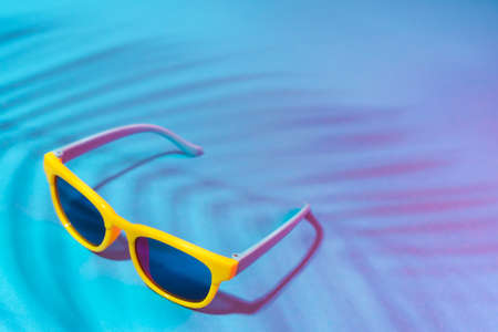 Minimalist photo of stylish yellow sunglasses with harsh shadow as summer concept. Close-up image of sunglasses on turquoise blue background in perspective. Moody summer photo with palm tree shadow.の写真素材