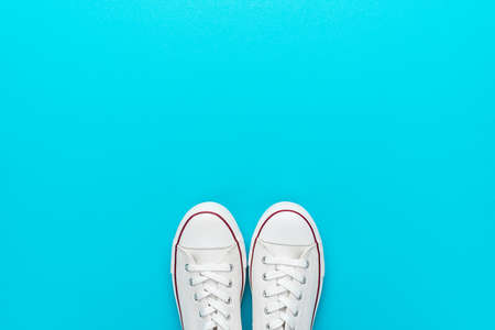 Minimalist flat lay image of white gumshoes over turquoise blue background with copy space. Flat lay...