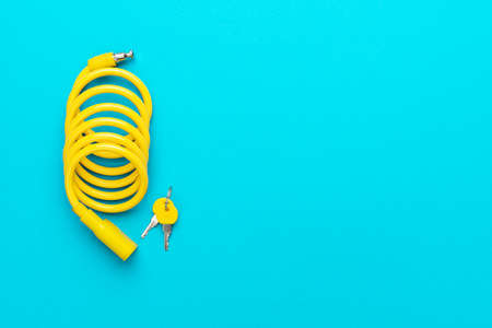 Yellow bike lock with keys over turquoise blue background. Top down flat lay photo of bicycle lock...