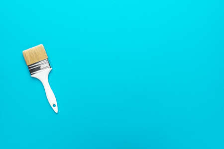 Paint brush on the turquoise blue background. Minimalist photo of white brush with copy space.
