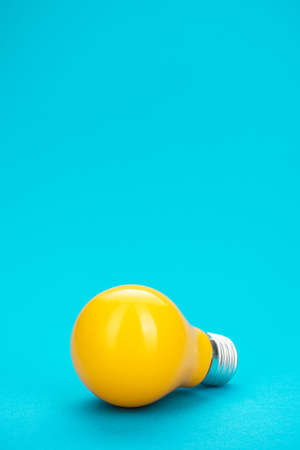 Yellow bulb on turquoise background with copy space. Minimalist photo of lightbulb over blue.