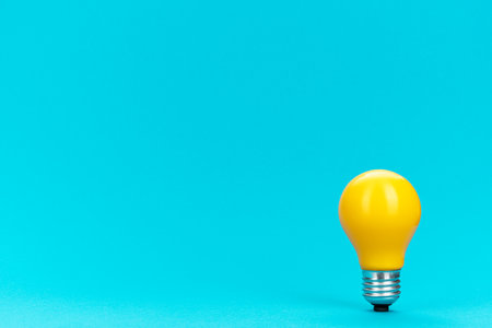 Yellow bulb standing on turquoise background with copy space. Minimalist photo of lightbulb over blue.の写真素材
