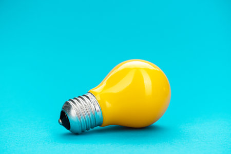 Yellow bulb on turquoise background with copy space. Minimalist photo of lightbulb over blue.