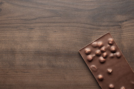 Chocolate bar with whole hazelnuts on brown table. Top view photo of chocolate on wooden background with copy space.の写真素材