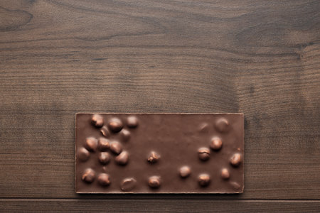 Chocolate bar with whole hazelnuts on brown table. Flat lay image of chocolate on wooden background with copy space.の写真素材