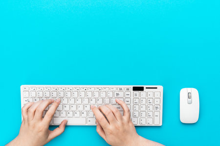 View from above on the office table with copy space. Minimalist photo of female hands typing on computer keyboard. Flat lay image of white computer peripherals over turquoise blue background.の写真素材