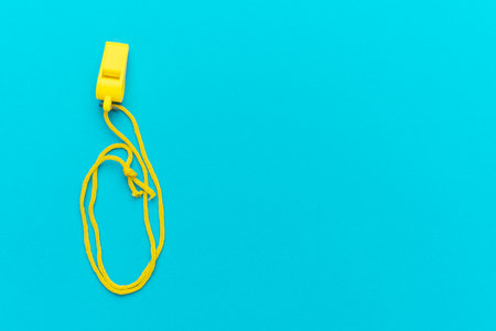Flat lay image of yellow referee whistle. Plastic referee whistle on turquoise blue background with copy space.の写真素材