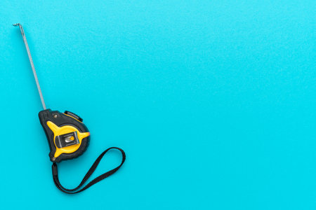 Minimalist photo of tape measure on turquoise blue background with copy space. Flat lay image of construction measuring tape.の写真素材