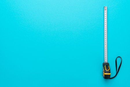 Top view minimalist photo of tape measure on turquoise blue background with copy space. Flat lay image of construction measuring tape.の写真素材