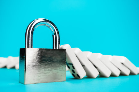 Standing padlock after domino effect chain reaction. Security concept with firmly standing closed lock with pile of fallen domino tiles in background. System toughness and stability concept.の写真素材