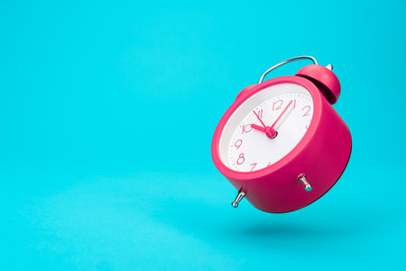Pink alarm clock in the air over turquoise blue background with copy space. Minimalist photo of...