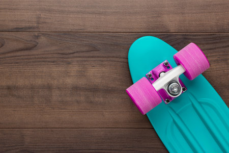 Flat lay photo of turquoise plastic mini cruiser skateboard with purple wheels on wooden background. Top view of bright turquoise cruiser skateboard with copy space.の写真素材