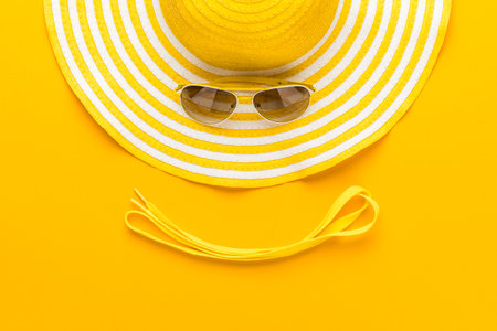 Top view of summer smiley face made with striped retro hat, sunglasses and shoe laces. Flat lay of beach hat and sunglasses on yellow background. Minimalist photo of summer vacation accessories.の写真素材