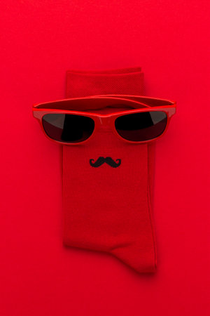 Vertical photo of red socks and red sunglasses making together funny little detective like or a cool dude character with moustache. Top view image of red socks and sunglasses on bright red background.の写真素材