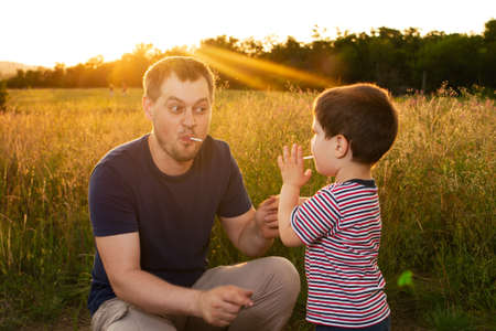 Dad and son walk in a yellow summer field in the evening at sunset and eat candy on a stick. Fathers Day, love in the family, the role of the father in raising the child.の写真素材
