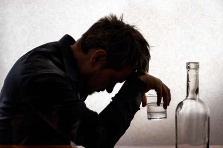 A silhouetted photo. A man in alcoholic intoxication holds a glass of alcohol. Alcoholism, addiction, deliriumの写真素材