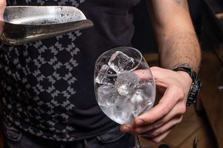 The bartender pours ice with an iron spatula into the glass. Ice cubes
