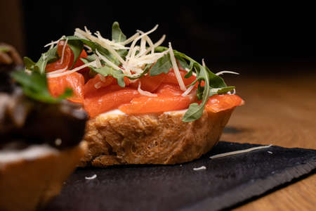Bruschetta from a French loaf with salmon, cheese and arugula. Snacks and sandwiches.