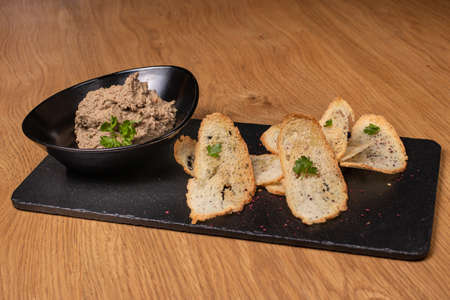 Pate of beef liver and meat with herbs in a black plate with crunchy toast. Restaurant food.